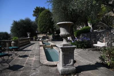 Massif de fleurs rouges et violettes entouré d'arbres et de verdure dans un jardin ensoleillé.