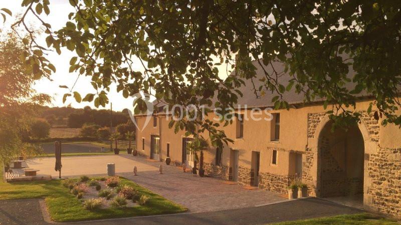 Bâtisse en pierre entourée de végétation, éclairée par une lumière douce au coucher du soleil.