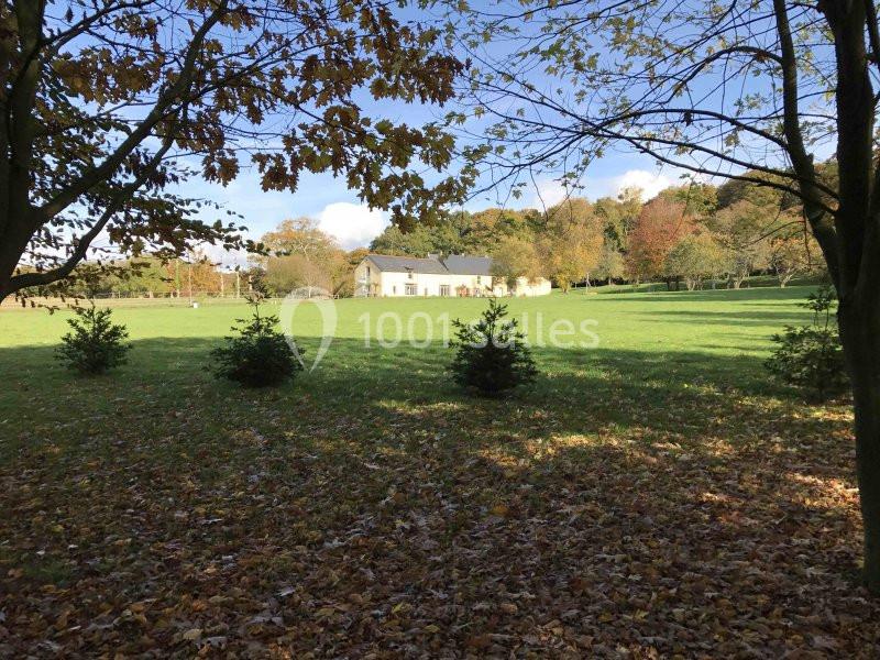 Vue d'une maison blanche entourée d'arbres et d'une pelouse verdoyante parsemée de feuilles d'automne.