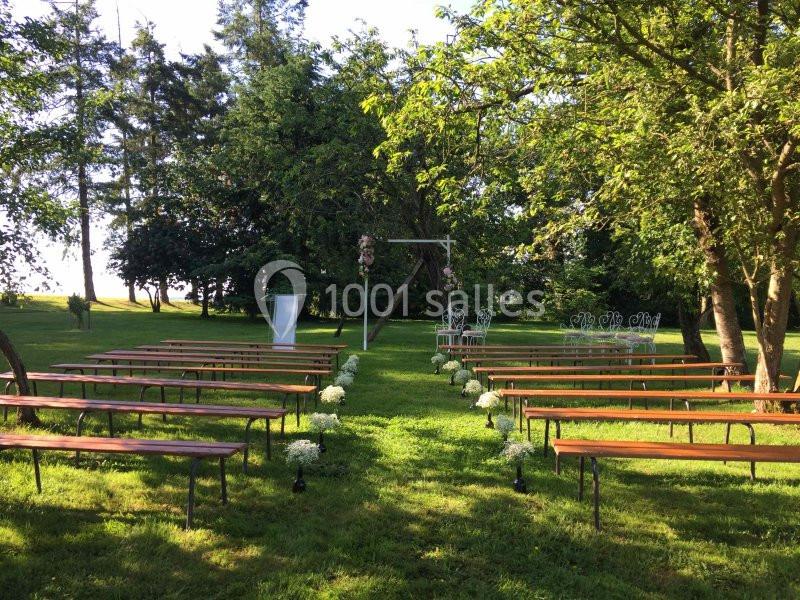 Allée centrale bordée de bancs en bois menant à une arche décorée, dans un jardin verdoyant et ensoleillé.
