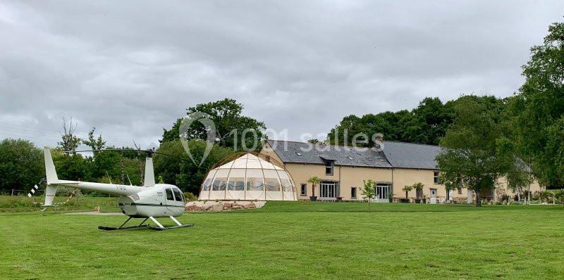 Hélicoptère posé sur une pelouse devant une maison avec un dôme géodésique adjacent, entourés de verdure.