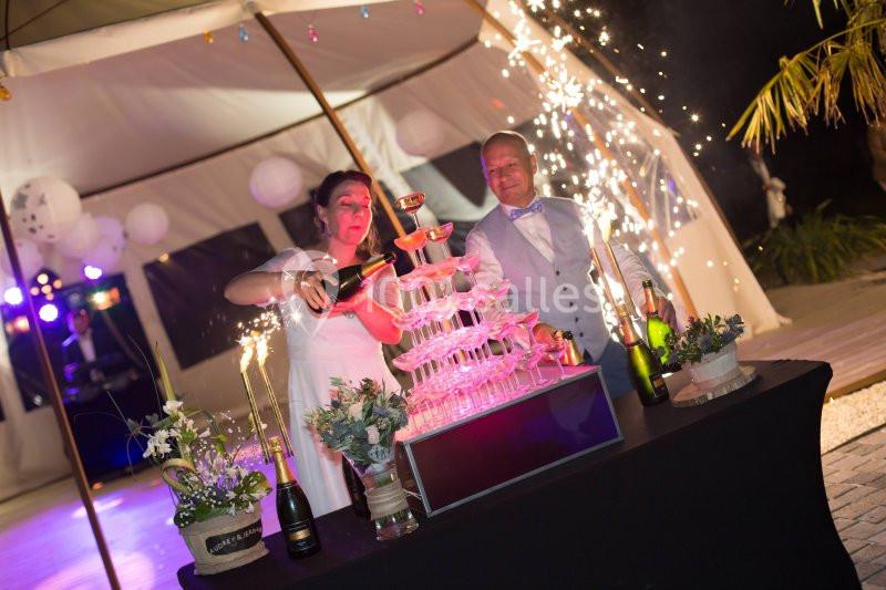 Un couple remplit une pyramide de coupes de champagne lors d'une célébration en soirée, entouré de décorations festives.