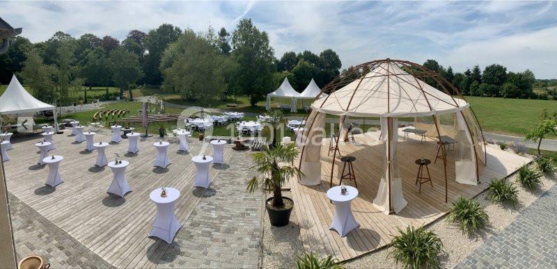 Espace extérieur aménagé avec tables hautes et chapiteaux dans un cadre verdoyant et ensoleillé.