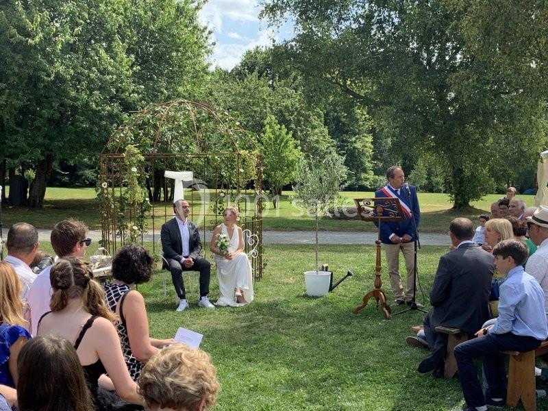Un couple assis lors d'une cérémonie de mariage en plein air, entouré d'invités et d'un officiant.