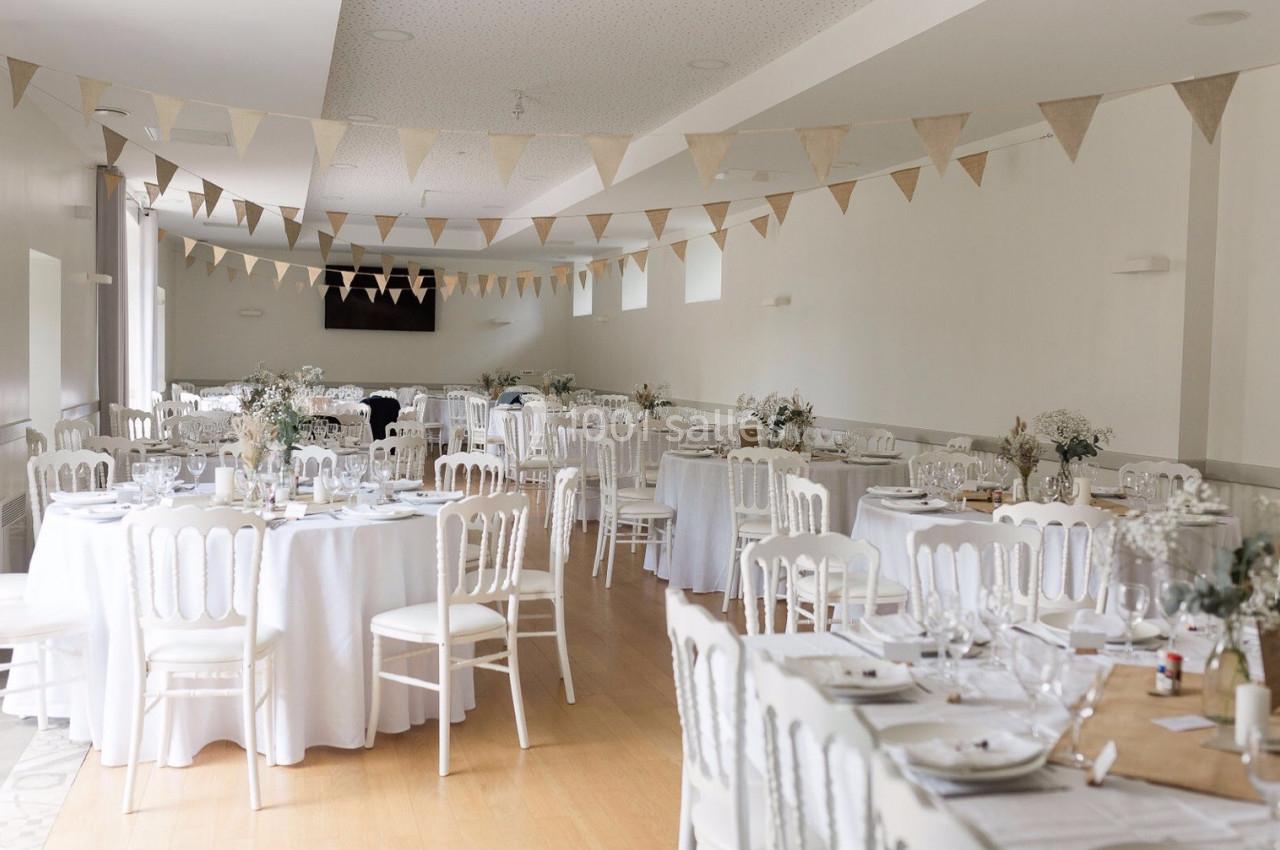 Salle de réception décorée avec des tables rondes dressées, des chaises blanches et des guirlandes de fanions suspendues.