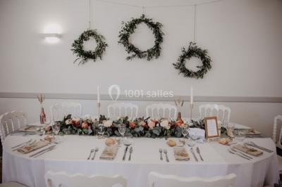 Centre de table floral avec fleurs séchées et pampas, entouré de couverts et cadeaux emballés sur une nappe blanche.