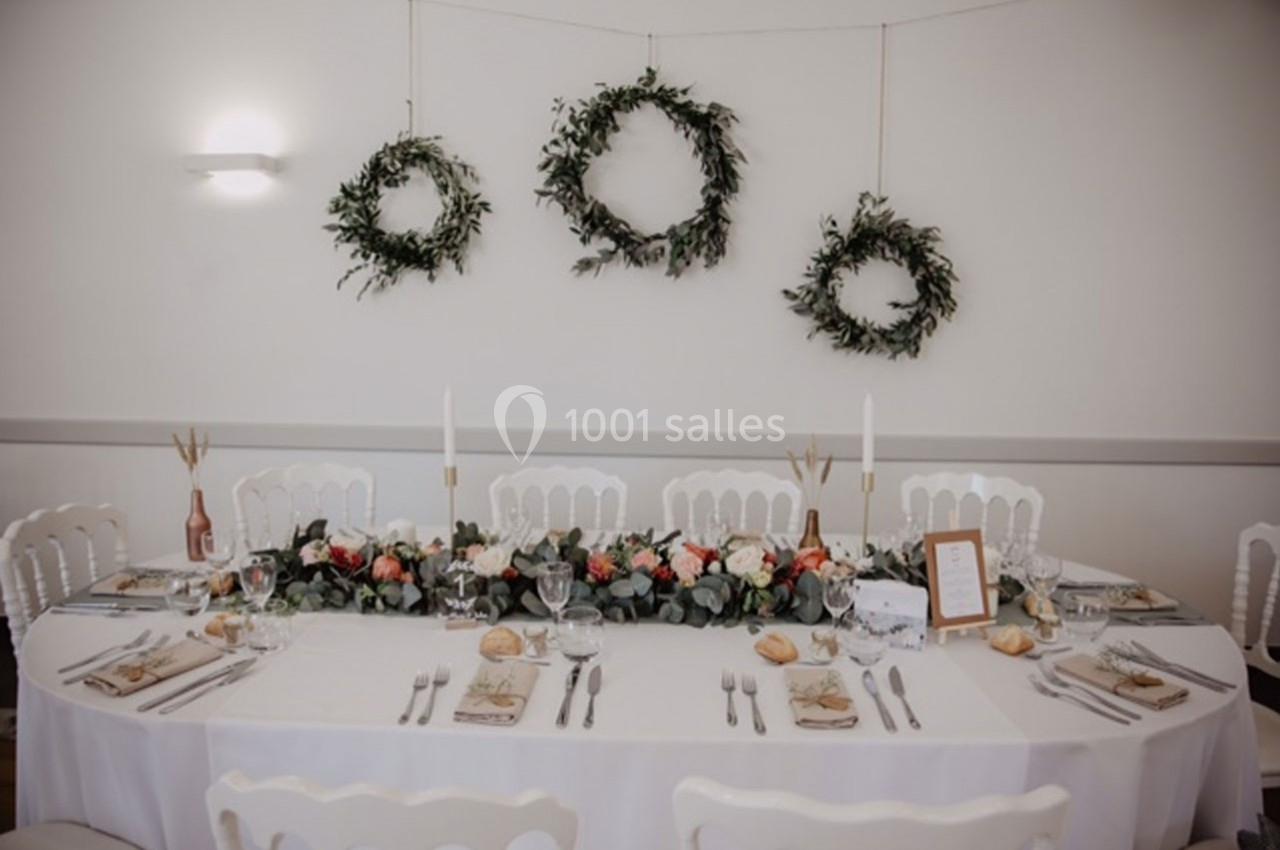 Table de réception élégamment dressée avec décoration florale centrale et couronnes végétales accrochées au mur.
