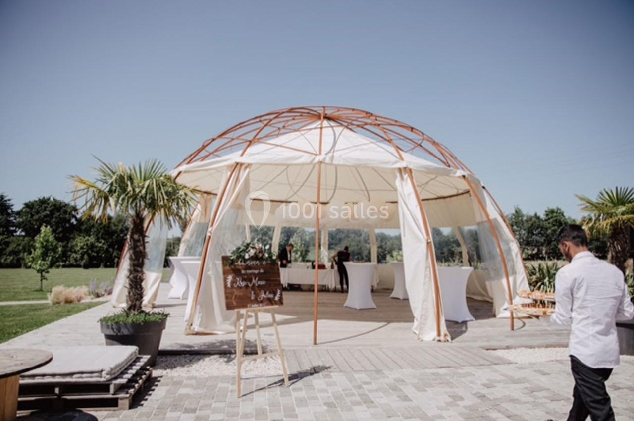 Structure en dôme avec toile blanche, entourée de palmiers, utilisée pour un événement en extérieur par temps ensoleillé.