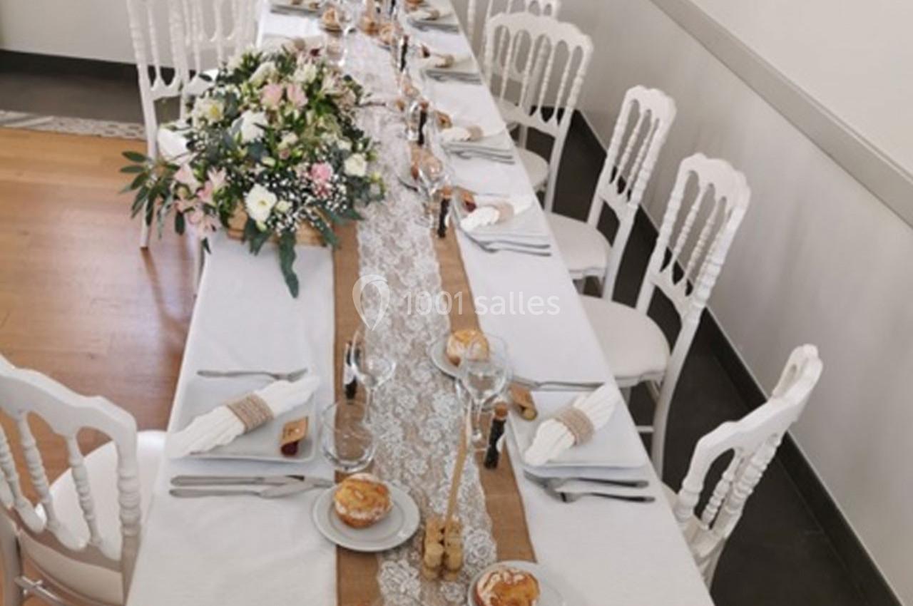 Table de réception décorée avec une nappe blanche, un chemin de table en dentelle, des fleurs et des couverts élégants.