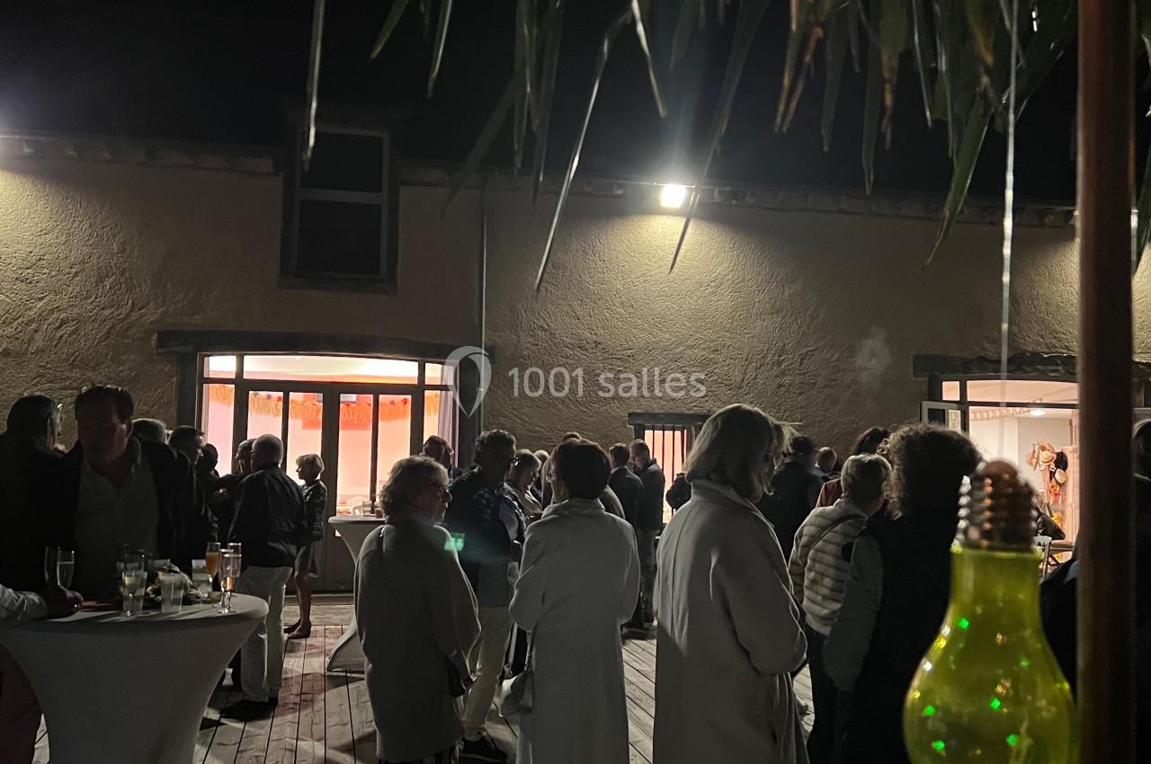 Groupe de personnes rassemblées en soirée sur une terrasse en bois, éclairée par des lumières suspendues.