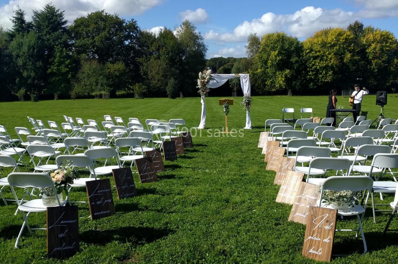 Chaises blanches disposées en rangées sur une pelouse pour une cérémonie en plein air, avec une arche décorée au centre.