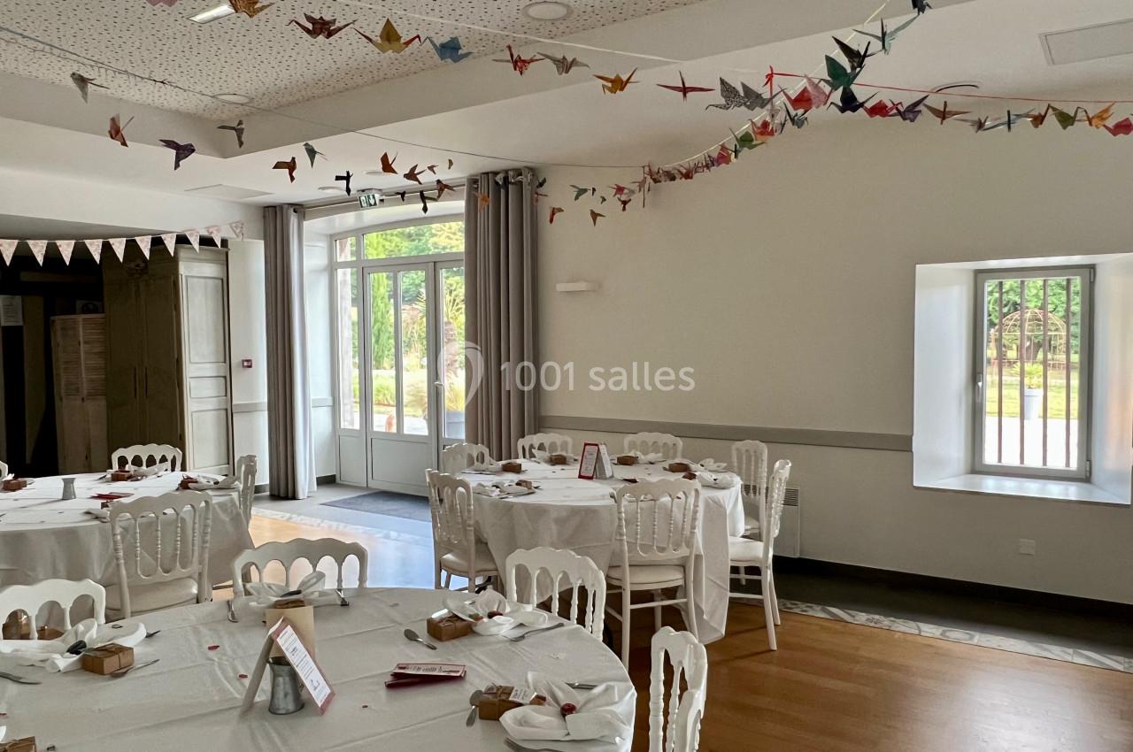 Salle de réception lumineuse décorée de guirlandes en origami, avec des tables rondes dressées pour un événement.