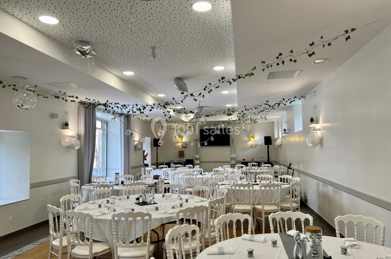 Salle de réception décorée avec des guirlandes végétales, des tables rondes dressées et des chaises blanches.
