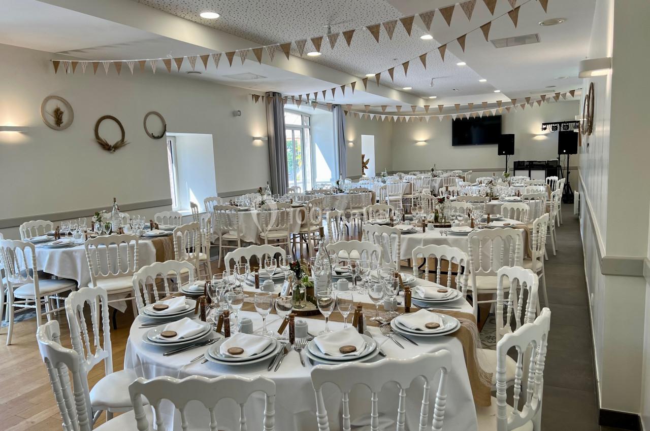 Salle de réception décorée avec des tables rondes dressées, des chaises blanches et des guirlandes en tissu suspendues.