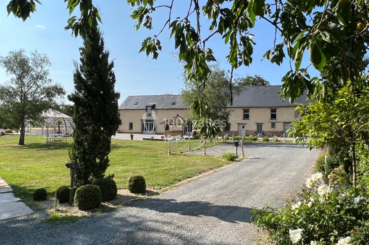 Allée gravillonnée menant à une grande maison en pierre entourée de pelouse et d'arbres sous un ciel dégagé.