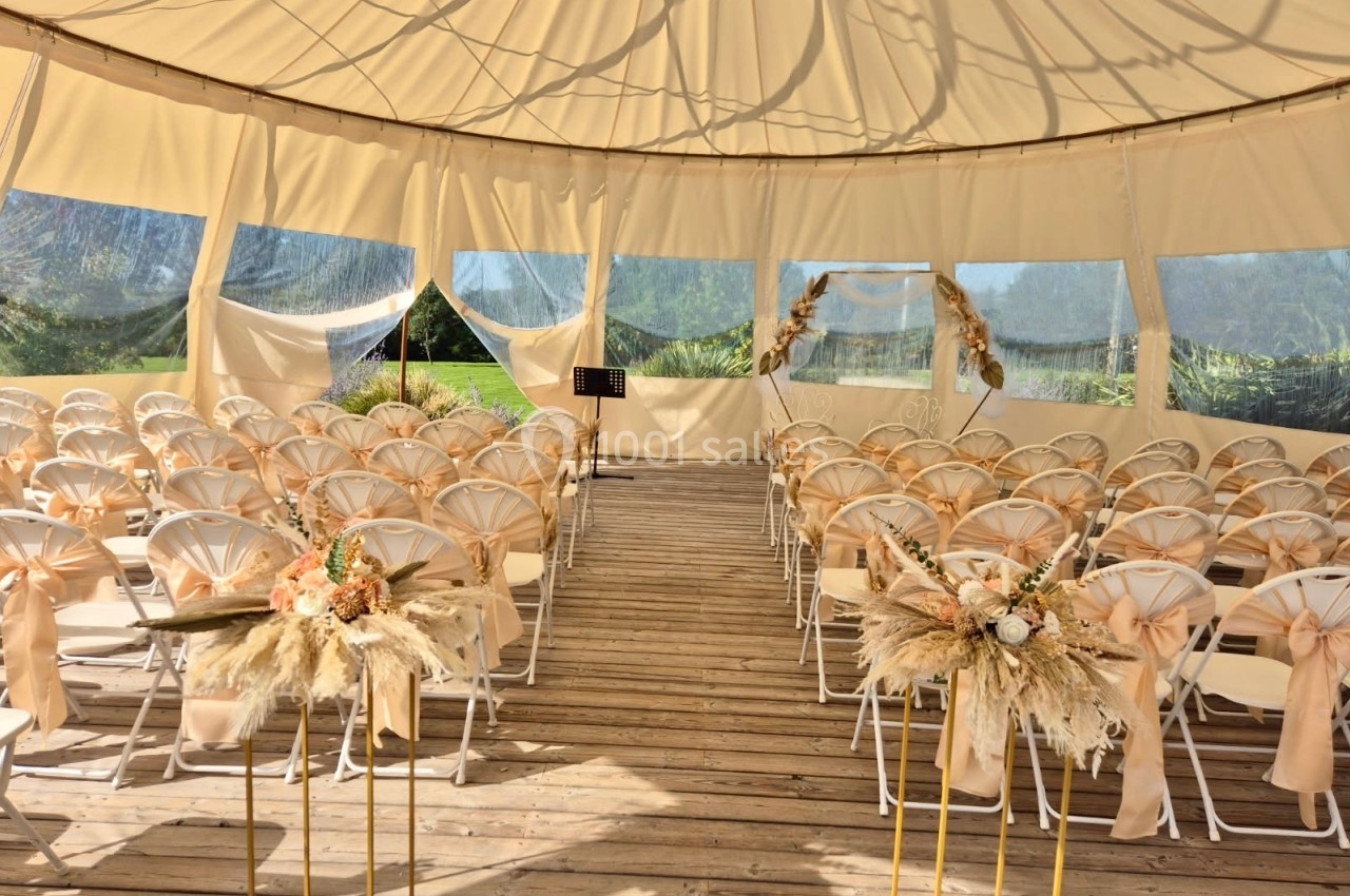 Salle de cérémonie en plein air sous une tente, avec des chaises décorées et des compositions florales.