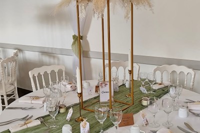 Centre de table floral avec fleurs séchées et pampas, entouré de couverts et cadeaux emballés sur une nappe blanche.