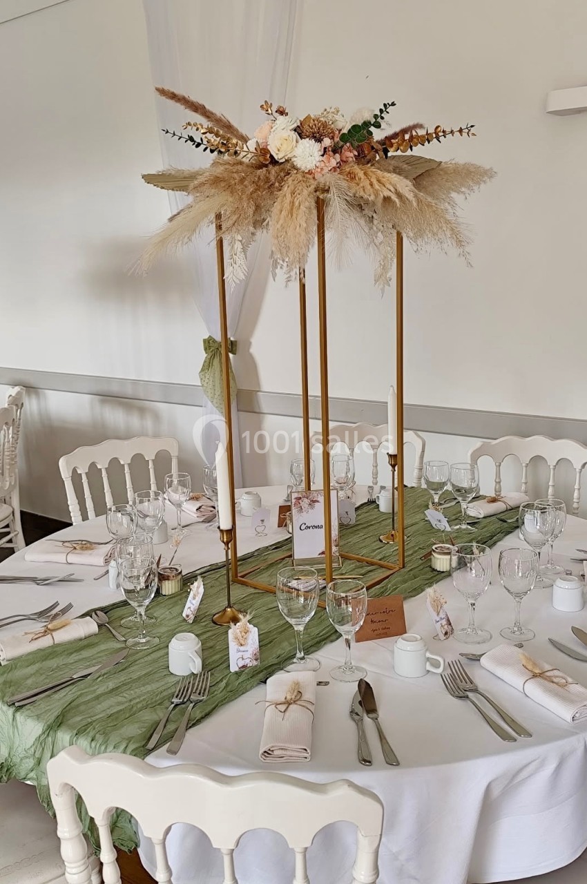 Table de réception décorée avec un centre de table floral, nappes vertes, vaisselle élégante et chaises blanches.