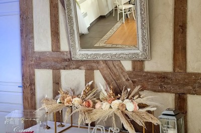 Centre de table floral avec fleurs séchées et pampas, entouré de couverts et cadeaux emballés sur une nappe blanche.