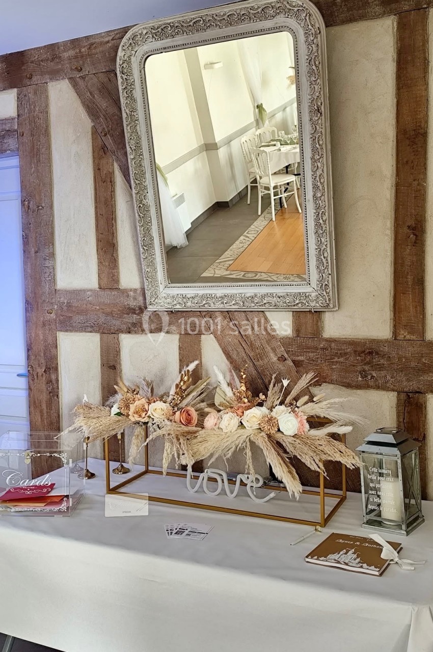 Décoration de table avec fleurs séchées, cadre ’love’, urne transparente et lanterne, dans une salle à colombages.
