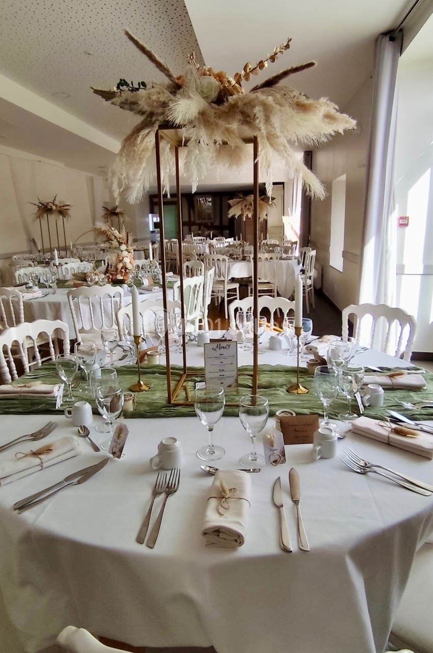 Salle de réception décorée avec des tables dressées, centre de table en fleurs séchées et vaisselle élégante.