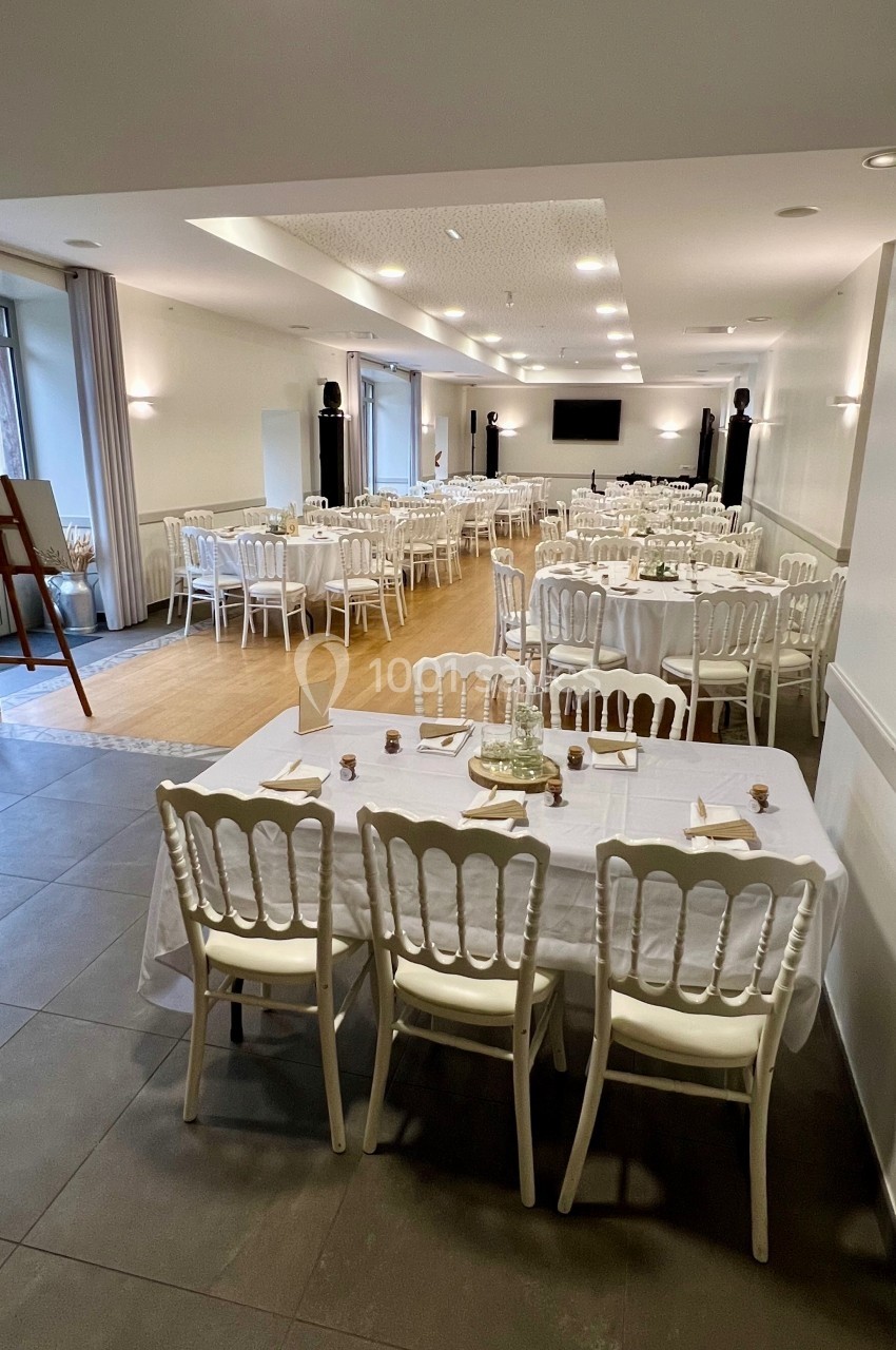 Salle de réception lumineuse avec tables dressées, chaises blanches et décoration sobre dans un cadre épuré.