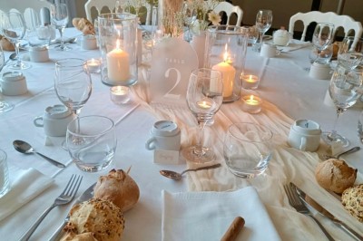 Centre de table floral avec fleurs séchées et pampas, entouré de couverts et cadeaux emballés sur une nappe blanche.