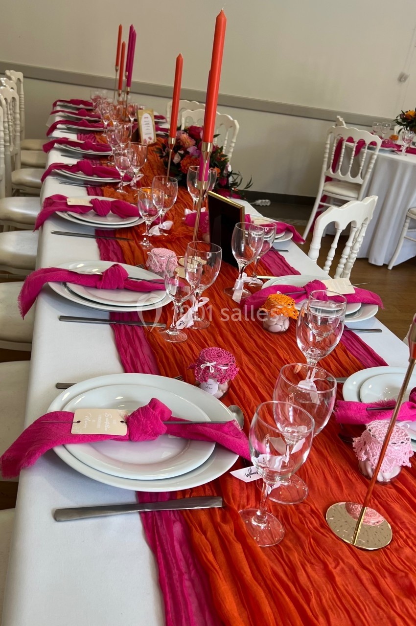 Table dressée avec une nappe orange, serviettes roses, chandeliers colorés et vaisselle élégante dans une salle de réception.