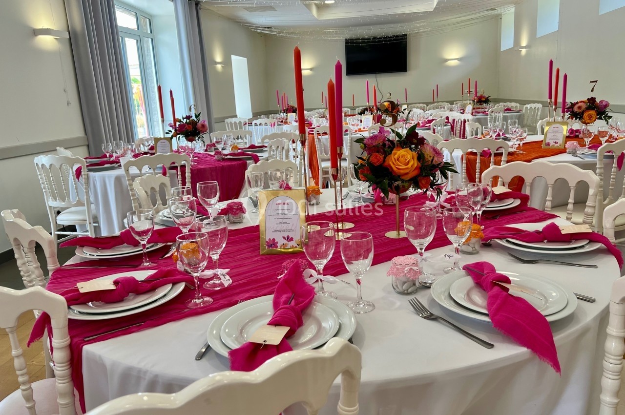 Salle de réception décorée avec des tables dressées, nappes blanches et roses, bougies rouges et compositions florales.
