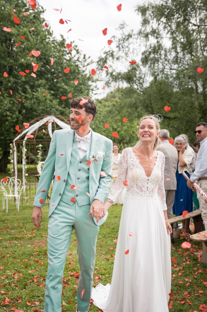 Un couple souriant marche sous une pluie de pétales rouges lors d'une cérémonie de mariage en extérieur.