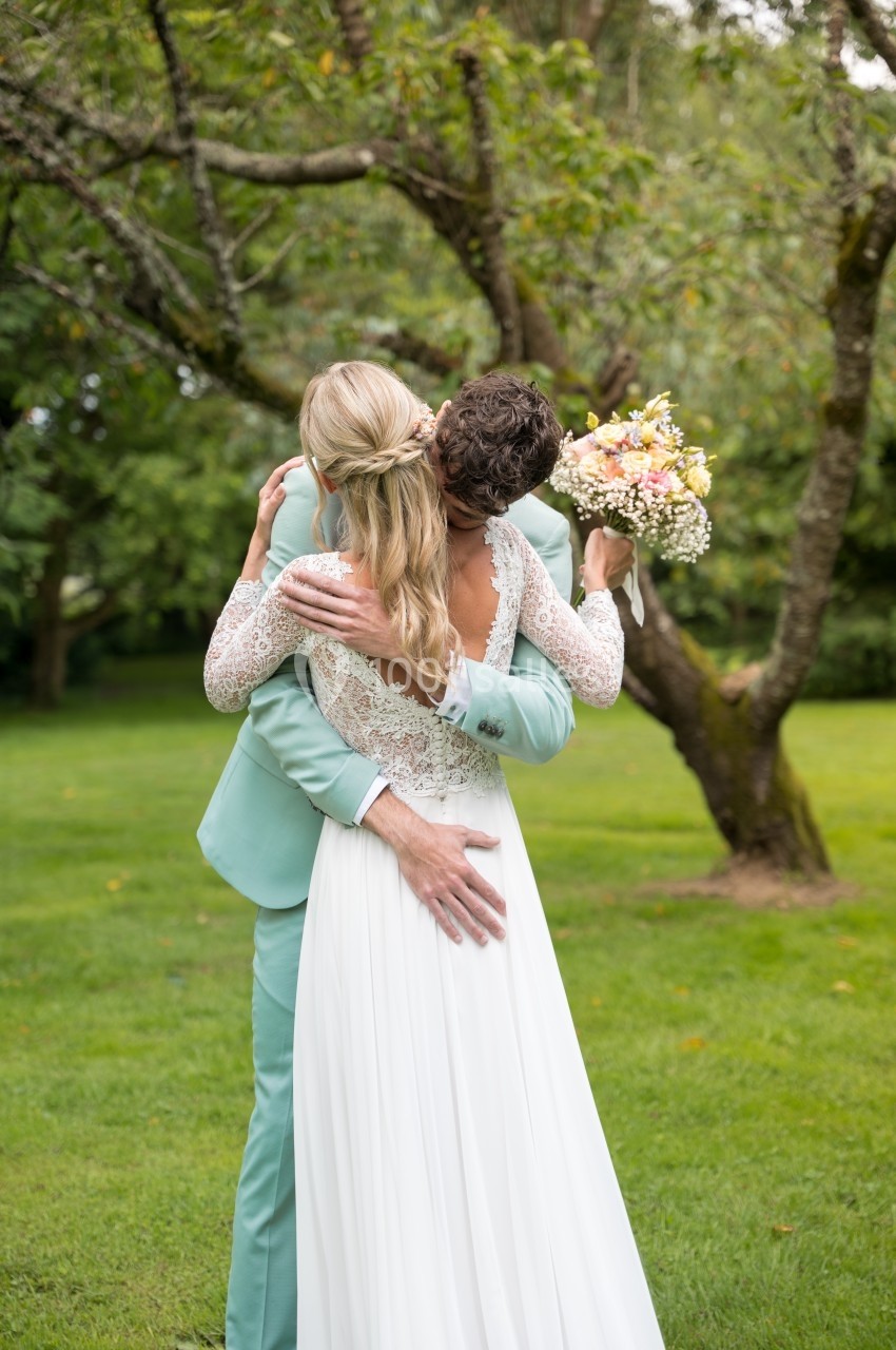 Un couple de mariés s'enlace dans un jardin, la mariée tenant un bouquet de fleurs pastel.