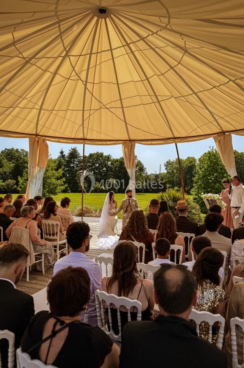 Cérémonie de mariage en extérieur sous une tente, avec les mariés face à l'officiant et des invités assis.