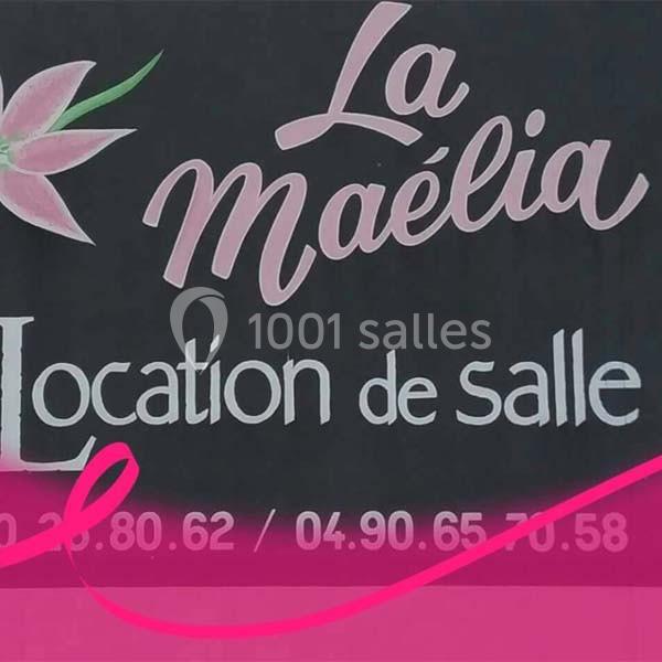 Panneau indiquant ’La Maélia - Location de salle’ avec un motif de fleur rose sur fond noir.