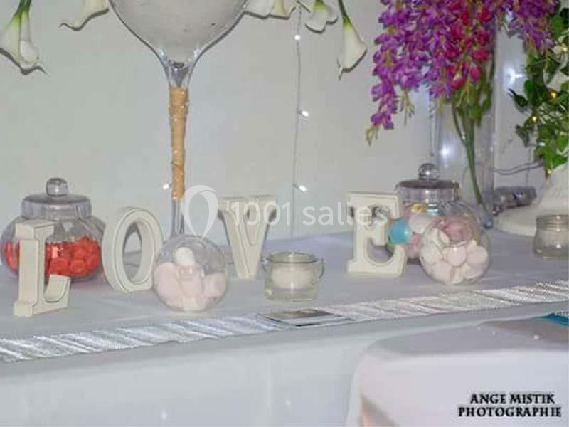 Décoration de table avec lettres formant ’LOVE’, bonbonnières remplies de sucreries et fleurs en arrière-plan.