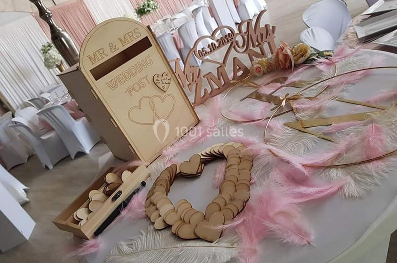 Décoration de table de mariage avec plumes roses, cœurs en bois et boîte aux lettres pour messages des invités.