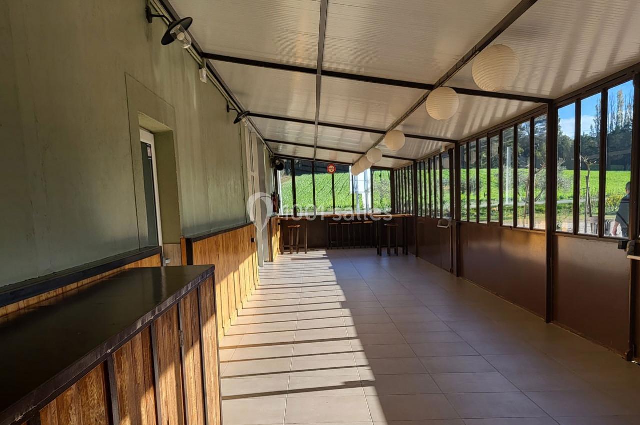 Véranda lumineuse avec murs en bois et grandes baies vitrées donnant sur un paysage de vignes.