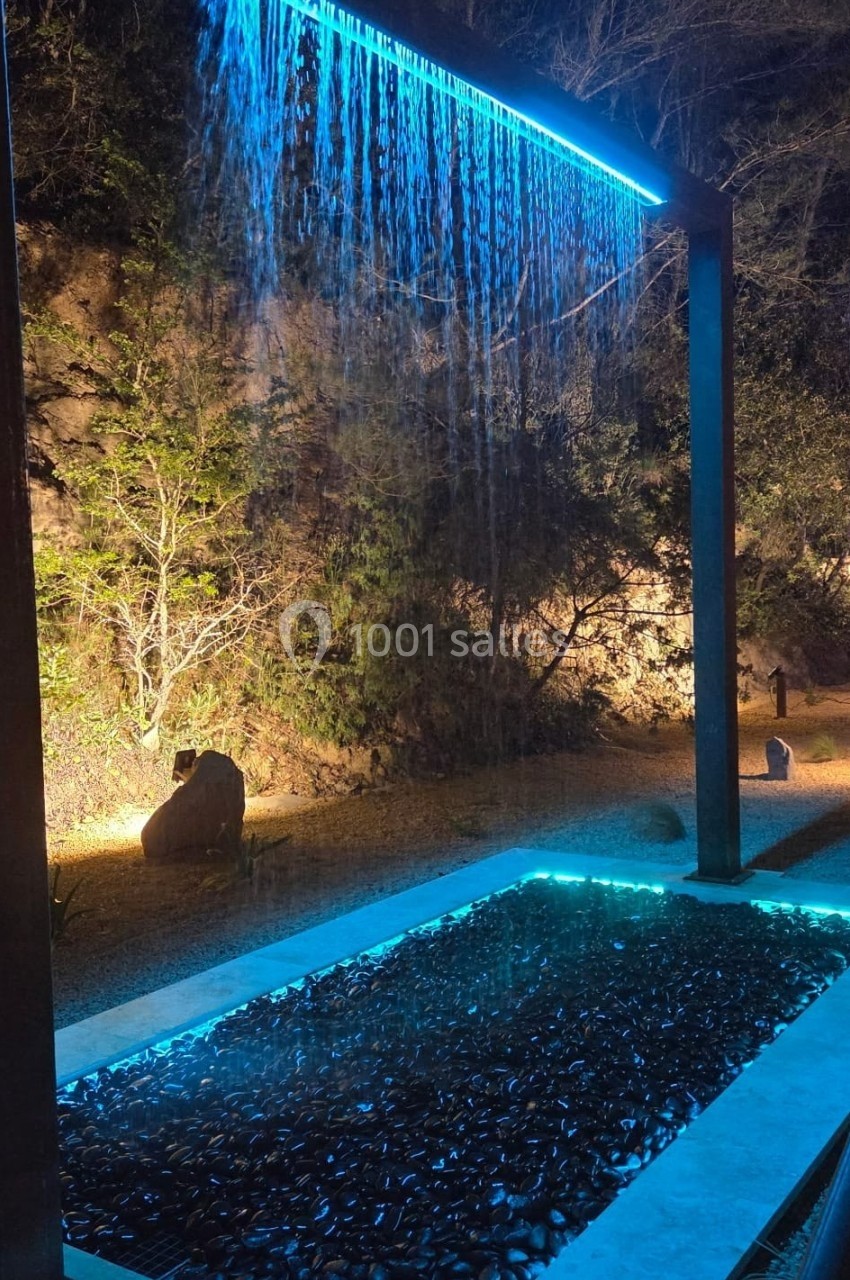 Location salle Loriol-du-Comtat (Vaucluse) - La Maelia #29 Cascade lumineuse tombant d'une structure métallique dans un bassin, entourée de végétation nocturne éclairée.