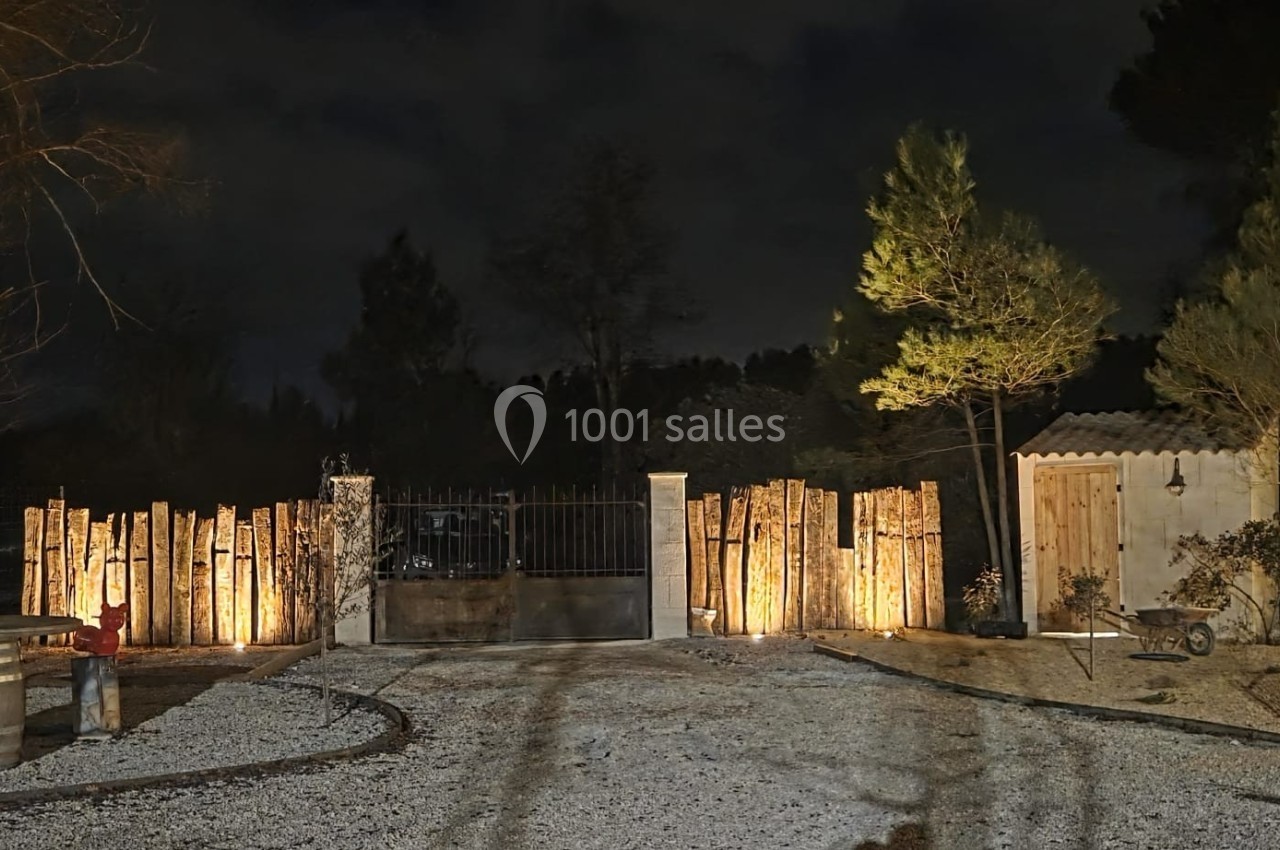 Location salle Loriol-du-Comtat (Vaucluse) - La Maelia #31 Entrée de propriété éclairée la nuit, avec portail en métal, clôture en bois et petite cabane sur la droite.