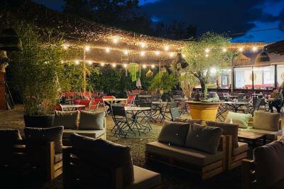 Miniature Location salle Saint-Priest (Rhône) - Le 21 #4 Salon de jardin extérieur avec canapé en palettes, table basse et plantes, devant une façade rouge avec porte en bois.