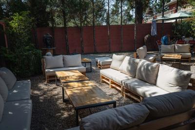 Miniature Location salle Saint-Priest (Rhône) - Le 21 #16 Salon de jardin extérieur avec canapé en palettes, table basse et plantes, devant une façade rouge avec porte en bois.