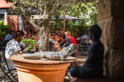Miniature Location salle Saint-Priest (Rhône) - Le 21 #17 Salon de jardin extérieur avec canapé en palettes, table basse et plantes, devant une façade rouge avec porte en bois.