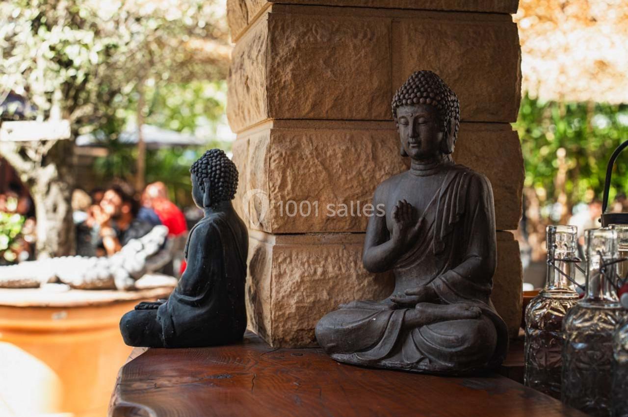 Deux statues de Bouddha en pierre posées sur une table en bois, avec un jardin en arrière-plan.