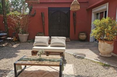 Miniature Location salle Saint-Priest (Rhône) - Le 21 #19 Salon de jardin extérieur avec canapé en palettes, table basse et plantes, devant une façade rouge avec porte en bois.