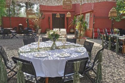 Miniature Location salle Saint-Priest (Rhône) - Le 21 #12 Salon de jardin extérieur avec canapé en palettes, table basse et plantes, devant une façade rouge avec porte en bois.