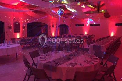 Salle de réception décorée avec des tables dressées, des fleurs et des voilages suspendus sous un plafond en bois.