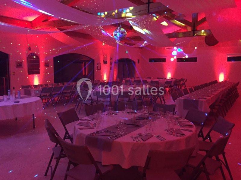 Salle de réception décorée avec des tables dressées, éclairage rouge tamisé et une boule à facettes au plafond.