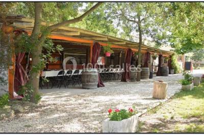 Salle de réception décorée avec des tables dressées, des fleurs et des voilages suspendus sous un plafond en bois.