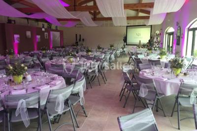 Salle de réception décorée avec des tables dressées, des fleurs et des voilages suspendus sous un plafond en bois.