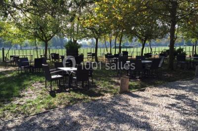 Salle de réception décorée avec des tables dressées, des fleurs et des voilages suspendus sous un plafond en bois.
