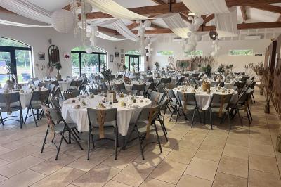 Salle de réception décorée avec des tables dressées, des fleurs et des voilages suspendus sous un plafond en bois.